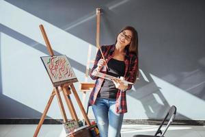 kreatives nachdenkliches malermädchen malt in der werkstatt ein buntes bild auf leinwand mit ölfarben foto