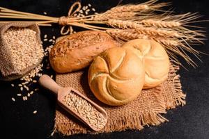 Schönes frisch gebackenes Brot mit Weizenkörnern auf dunklem Betonhintergrund foto