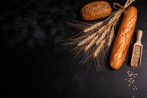 Schönes frisch gebackenes Brot mit Weizenkörnern auf dunklem Betonhintergrund foto