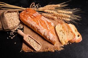 Schönes frisch gebackenes Brot mit Weizenkörnern auf dunklem Betonhintergrund foto