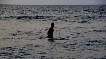 dokumentation von surfern in aktion in der dämmerung mit goldener farbe und dunkel, unscharf und dunkel am strand von senggigi lombok, west nusa tenggara indonesien, 27. november 2019 foto