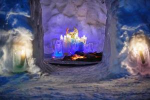 Installation zum Thema Weihnachten im Inneren des Schneehauses mit bunten eisigen Plafonds und brennenden Kerzen darin in kalter Winternacht. Blick durch die Tür. foto