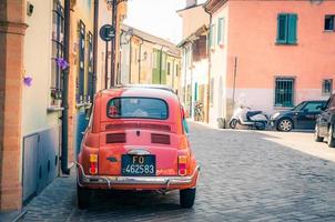 rimini, italien, 19. september 2018 retro oldtimer fiat 500 l rot geparkt auf kopfsteinpflasterstraße mit typisch italienischen alten gebäuden mit bunten wänden und traditionellen häusern im historischen stadtzentrum foto