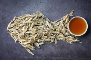 Fischsauce auf weißer Schüssel und kleiner getrockneter Fisch auf dunklem Hintergrund, Fischsauce aus Fermentationsfischen oder kleinen Wassertieren, fermentierte Lebensmittel foto