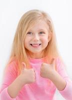 Nahaufnahmeporträt eines netten, fröhlichen, kleinen Mädchens, das doppelte Daumen nach oben zeigt foto