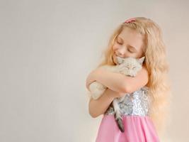kleines glückliches blondes mädchen umarmt ein beiges schlafendes kätzchen und lächelt und schließt ihre augen. foto