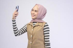 Portrait der schönen Frau mit Hijab mit Handy auf weißem Hintergrund foto