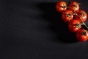 Zweig der roten Bio-Tomaten auf schwarzem Hintergrund. foto