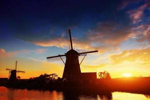 Landschaft mit schöner traditioneller holländischer Mühle in der Nähe von Wasserläufen mit fantastischem Sonnenuntergang und Reflexion im Wasser. Niederlande. foto