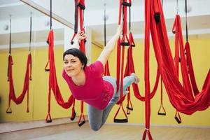 junge schöne frau, die yoga-fliege mit einer hängematte im studio praktiziert. foto