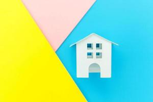 einfach design mit miniatur-weißem spielzeughaus isoliert auf blau gelb rosa pastell bunt trendy geometrischen hintergrund hypotheken-sachversicherung traumhaus konzept. flach liegend draufsicht kopierraum. foto