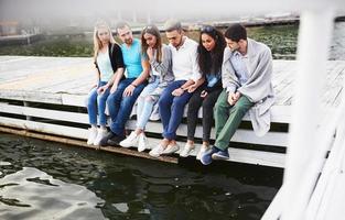 Porträt glücklicher junger Freunde, die auf einem Pier am See sitzen foto