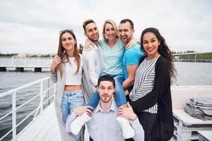 Porträt einer Gruppe junger Menschen, die am Rand der Seebrücke sitzen, draußen in der Natur. Freunde, die ein Spiel auf dem See genießen. foto