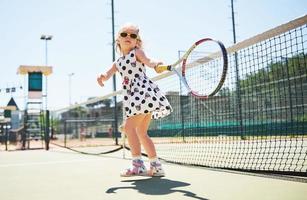 süßes kleines Mädchen, das draußen auf dem Tennisplatz Tennis spielt foto