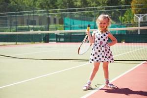 süßes kleines Mädchen, das draußen auf dem Tennisplatz Tennis spielt foto