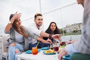 Glückliche junge Freunde saßen an einem Tisch und machten ein Picknick im Freien foto