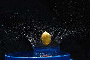 gelbe zitrone, die in das blaue wasser auf schwarzem hintergrund fällt foto