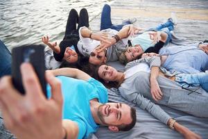 Porträt glücklicher junger Freunde auf dem Pier am See. während Sie den Tag genießen und Selfies machen. foto