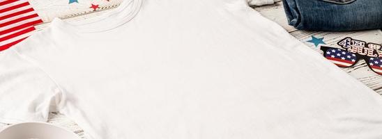 weißes t-shirt des modelldesigns für logo, hochwinkelansicht auf weißem hölzernem hintergrund mit us-flagge, schuhen und jeans foto