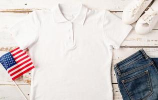 weißes polo-t-shirt des modelldesigns für logo, draufsicht auf weißem hölzernem hintergrund mit us-flagge, schuhen und jeans foto