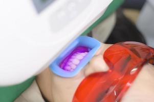 eine Frau mit Schutzbrille, die vom Stomatologen untersucht wird, Zahnaufhellung durch UV-Lampe foto