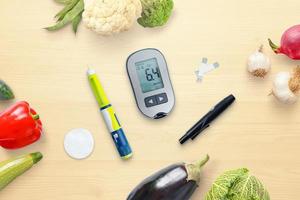 Diabetes-Konzept-Zusammensetzung mit Blutzuckermessgerät und Insulin, umgeben von gesunder Ernährung, Gemüse. Ansicht von oben, flach liegend foto
