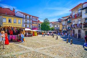 menschen touristen, die den gepflasterten platz mit traditionellen bunten häusern im historischen zentrum der stadt guimaraes hinuntergehen foto