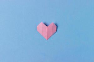 Herz aus rosa Papier in Origami-Technik auf blauem Hintergrund gefaltet. ein Objekt. konzept der liebe, feier, pflege, gesundheit, leben