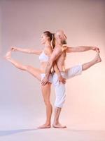 Schöne sportliche Frau und Mann in weißen Kleidern, die gemeinsam Yoga-Asanas im Innenbereich machen foto