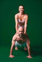 Schöne sportliche Frau und Mann in weißen Kleidern, die gemeinsam Yoga-Asanas im Innenbereich auf grünem Hintergrund machen foto