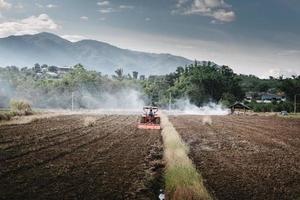 Landarbeiter fuhren Traktor für die Bodenbearbeitung auf landwirtschaftlichen Feldern. landwirt, der bodenpflugvorbereitung auf traktormaschine für pflanzenanbau bearbeitet. Ländliche Landschaft von landwirtschaftlichem Ackerland während des Sonnenuntergangs foto