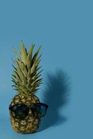 lustige ananas in cooler sonnenbrille auf blauem hintergrund. hinterer dunkler Schatten. foto