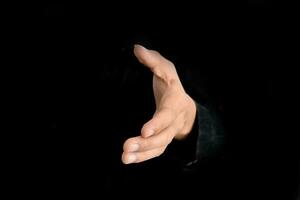 Geschäftsmann bietet Hand für Händedruck und Zusammenarbeit auf schwarzem Hintergrund. Geschäftsvorschlagskonzept. foto