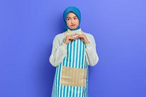 Porträt einer nachdenklichen jungen Hausfrau in Hijab und Schürze, die ernsthaft über eine Frage nachdenkt, die auf violettem Hintergrund isoliert ist. Menschen Hausfrau muslimischen Lifestyle-Konzept foto
