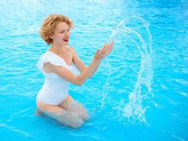 lächelndes rothaariges Frauenporträt, das das Leben im weißen Badeanzug im Schwimmbad genießt foto