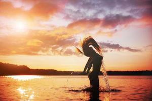 junges, schönes Mädchen, das bei Sonnenuntergang am Strand spazieren geht. stilvolle Frau mit langen Haaren, die in Bluse und Jeans-Shorts steht foto