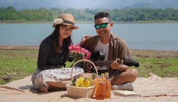 glückliches junges Paar, das im Urlaub am See Gitarre spielt foto