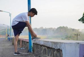 junger asiatischer mann bereitet seine schuhe vor dem morgendlichen joggen vor foto