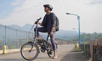 asiatischer junger mann mit rucksack, der sich nach der fahrradfahrt ausruht foto