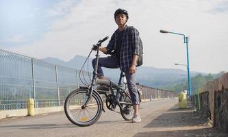 asiatischer junger mann mit rucksack, der sich nach der fahrradfahrt ausruht foto