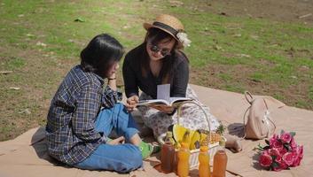 zwei glückliche junge asiatische frauen, die ein buch lesen, während sie am see urlaub machen foto