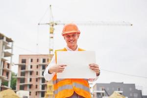 architektur- und hausrenovierungskonzept - mann in helm und handschuhen mit bauplan in der fabrik foto