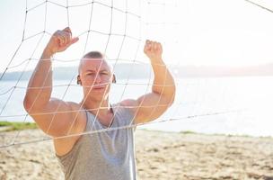 Ein sportlicher Mann, der am wilden Sandstrand auf das Meer blickt. maskuliner und sportlicher mann mit nacktem oberkörper macht abendtraining an der meeresküste. Sommer-Workout-Training im Freien foto