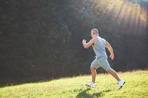 Fitness-Mann-Athlet, der bei Sonnenuntergang in der Natur joggt. Person, die im Sommer in Sportbekleidung und Schuhen einen aktiven Lebensstil trainiert und Cardio trainiert. foto