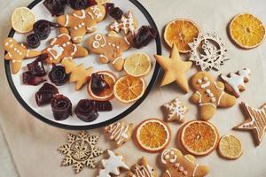 weihnachtslebkuchenplätzchen und getrocknete orange und gewürze auf weißem tisch. Pastell, Marmelade in Rollen auf einem Teller foto