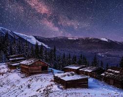magische winterschneebedeckte bäume und bergdorf. Winterlandschaft. lebendiger Nachthimmel mit Sternen und Nebel und Galaxien. foto