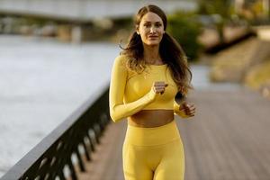 junge Frau, die auf dem Pier am Flussufer läuft foto