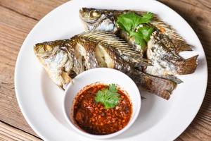 gekochtes Essen gegrillter Tilapia-Fisch - Tilapia-Süßwasserfisch auf weißem Teller mit Chilisauce foto