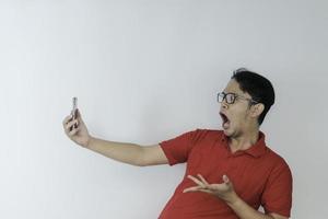 wow gesicht des jungen asiatischen mannes schockiert, was er im smartphone auf isoliertem grauem hintergrund sieht. foto