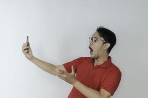wow gesicht des jungen asiatischen mannes schockiert, was er im smartphone auf isoliertem grauem hintergrund sieht. foto